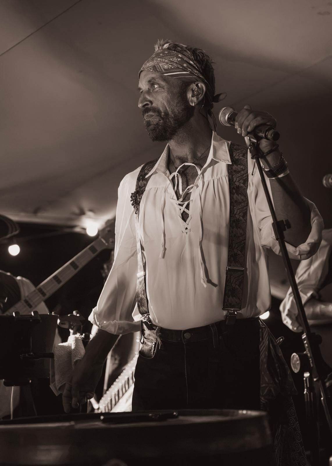 The frontman in a loose white shirt and bandana at the microphone